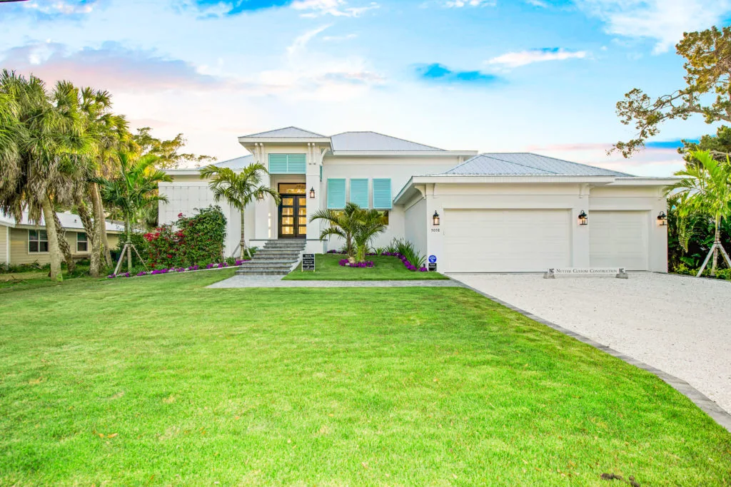 Nutter Custom Construction coastal-style custom home exterior in Sarasota, FL, with metal hip roof, aqua shutters, and three-car garage